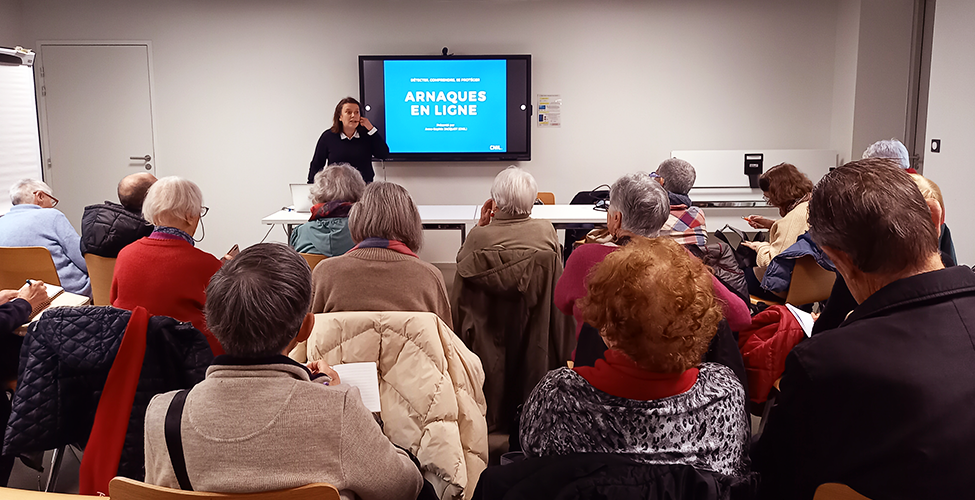 Photographie d'une conférence. Dans une salle, un agent la CNIL, face caméra, présente des diapositives sur un écran face à un public de dos.
